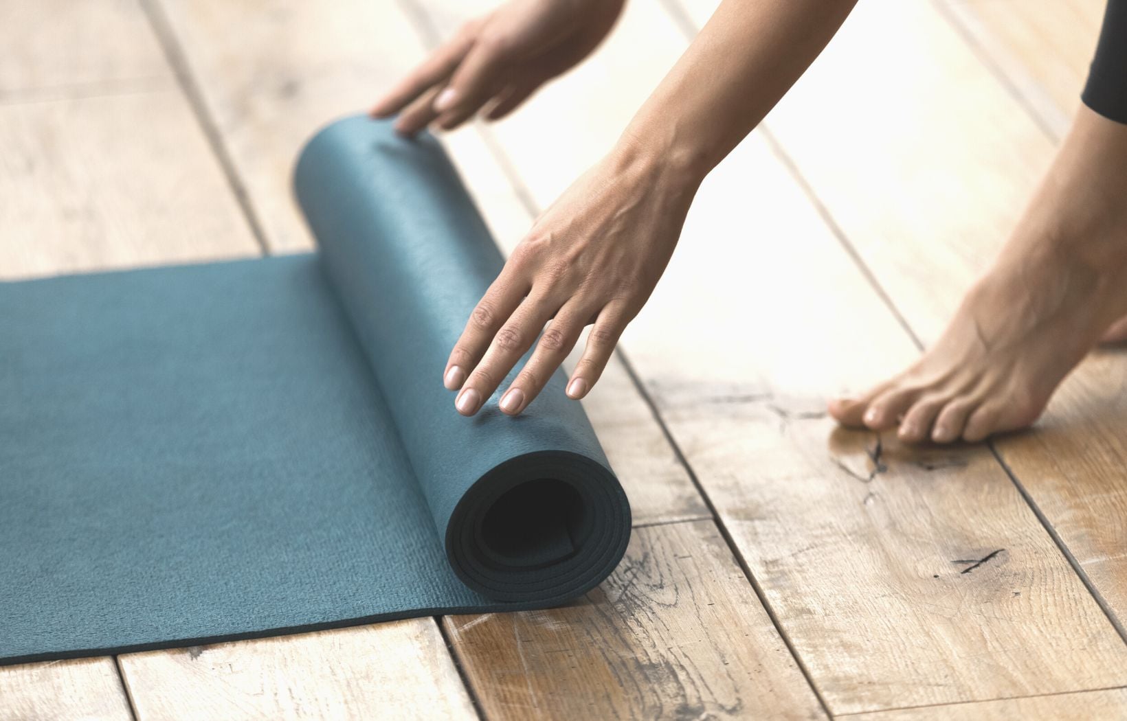 Close up of green pilates mat being rolled out on the floor by a woman's hands.